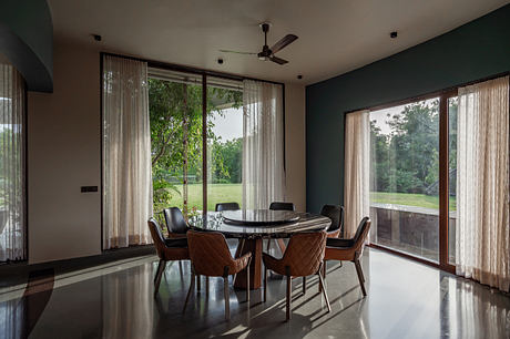 Elegant dining area with dark walls, large windows, and a round marble table surrounded by leather chairs.