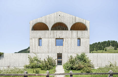 A concrete building with three large arched windows and a staircase leading to the entrance.