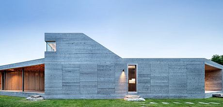 A modern, angular building with a slate-gray exterior and large windows, set against a grassy landscape.