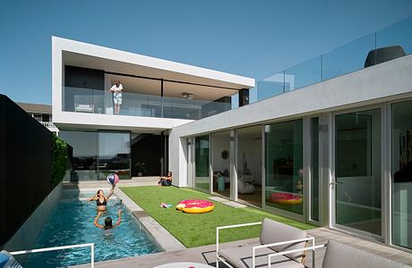 Modern, glass-walled home with sleek, minimalist design, pool, and lush landscaping.