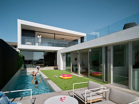 Modern, glass-walled home with sleek, minimalist design, pool, and lush landscaping.