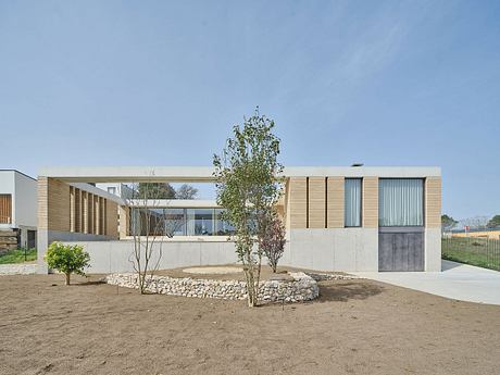 Modern single-story building with wood and concrete facade, surrounded by landscaping.