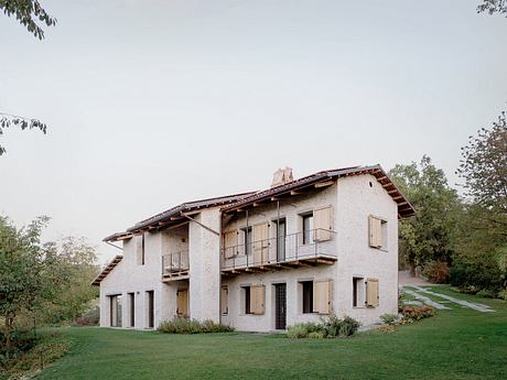 A stucco building with a slanted roof, balconies, and surrounded by lush greenery.