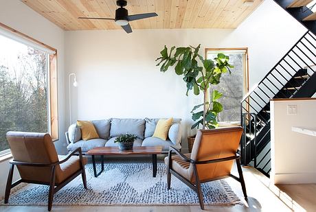 Cozy living room with wooden ceiling, large windows, modern furniture, and potted plant.