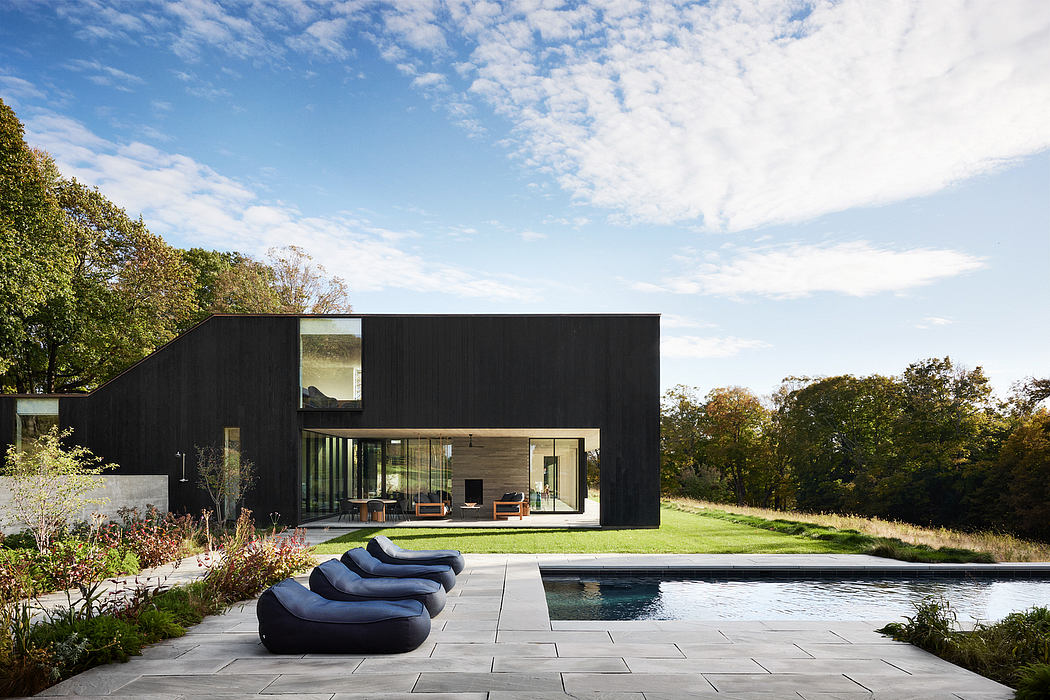 An architecturally striking modern home with a sleek black exterior, expansive windows, and a pool.