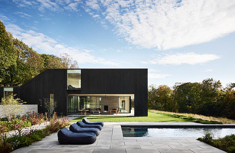 An architecturally striking modern home with a sleek black exterior, expansive windows, and a pool.