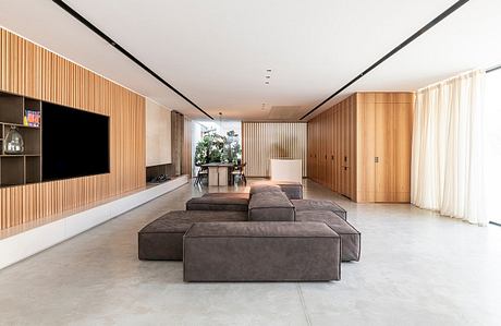 Spacious, minimalist living room with wooden paneling, large sectional sofa, and TV.