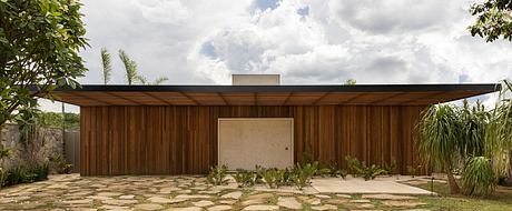 A modern wooden structure with a pitched roof, surrounded by lush greenery and a stone pathway.