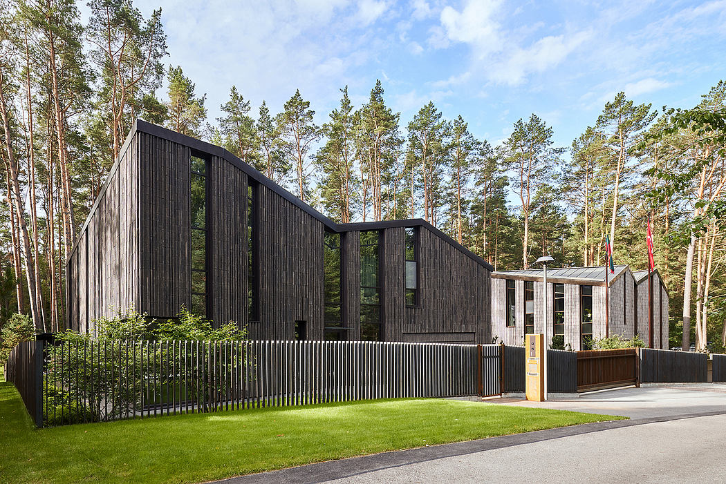 A modern, angular building with dark wood siding and large glass windows, surrounded by pine trees.