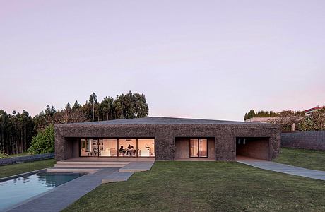 Contemporary single-story house with flat roof, glass walls, and pool in grassy yard.