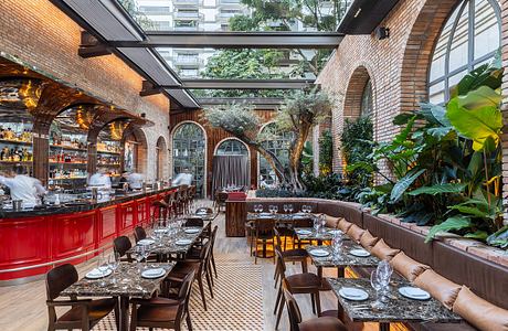 A lush indoor garden setting with brick arches, tropical foliage, and a vibrant red bar.