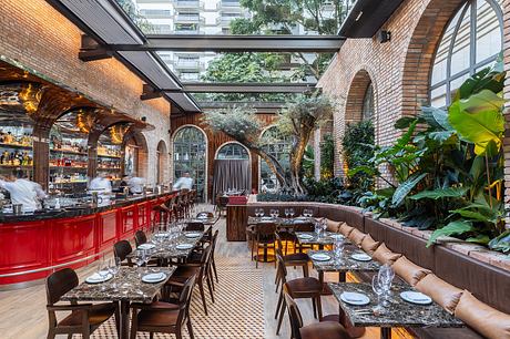 A lush indoor garden setting with brick arches, tropical foliage, and a vibrant red bar.