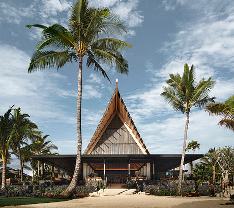 Tropical resort with distinctive triangular roof and open-air design, surrounded by palm trees.