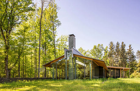 A modern glass and wood cabin nestled in a lush, green forest with a tall chimney.