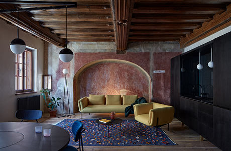 Warm, rustic interior with wood-beamed ceiling, arched stone niche, and patterned rug.