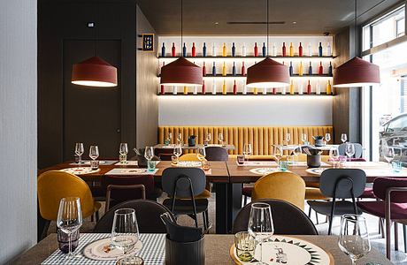 Modern restaurant interior featuring pendant lamps, wine shelves, and patterned plates on wooden tables.