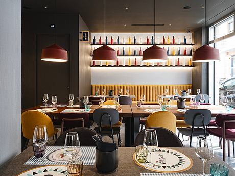 Modern restaurant interior featuring pendant lamps, wine shelves, and patterned plates on wooden tables.
