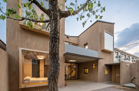 An architecturally striking modern building with wooden facade, intriguing windows, and a large tree.