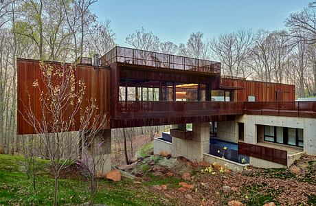 A contemporary, wood-clad home with large windows and a raised deck, nestled in a forested setting.