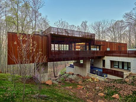 A contemporary, wood-clad home with large windows and a raised deck, nestled in a forested setting.