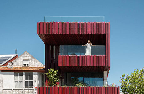 Modern multi-story building with vibrant red wood panels and glass windows, featuring a balcony.