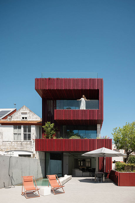 Modern multi-story building with vibrant red wood panels and glass windows, featuring a balcony.