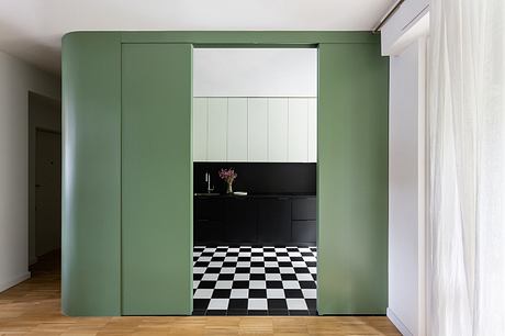 A modern kitchen with sleek green cabinets, checkered floor tiles, and bright natural light.