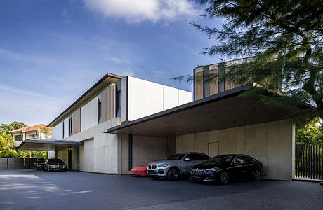 A modern, sleek residential building with a covered carport and two luxury vehicles parked.