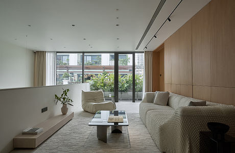 Modern living room with lush greenery visible through glass doors, sleek furniture and lighting.