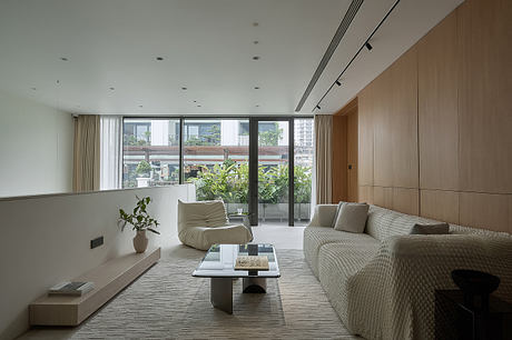 Modern living room with lush greenery visible through glass doors, sleek furniture and lighting.