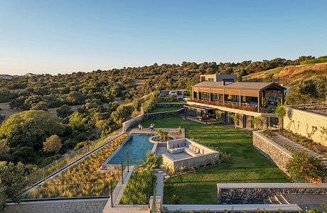 Modern two-story building with sleek roof design overlooking a lush landscaped property featuring a pool, pathways, and terraces.