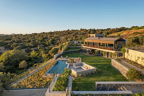 Modern two-story building with sleek roof design overlooking a lush landscaped property featuring a pool, pathways, and terraces.