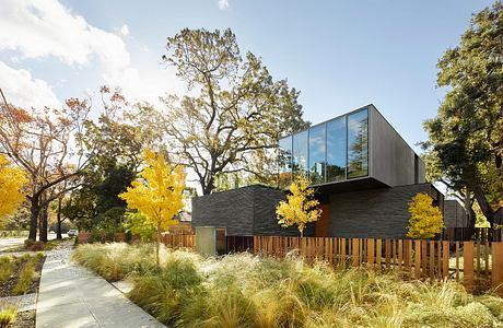 Modern architectural design with wooden fence, lush landscaping, and fall foliage.