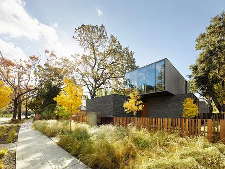 Modern architectural design with wooden fence, lush landscaping, and fall foliage.