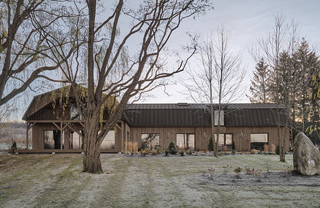 A rustic wooden building with a pitched roof and covered patio, surrounded by barren trees.