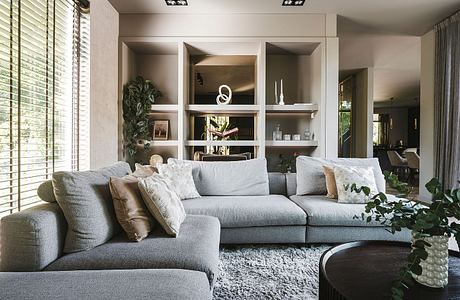 Cozy living room with plush gray sectional, shelves, and greenery accents.