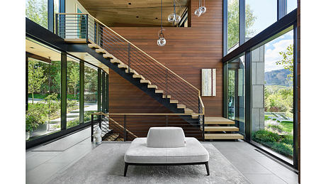 A modern, open-concept interior with a sleek staircase, wood paneling, and large windows offering scenic views.