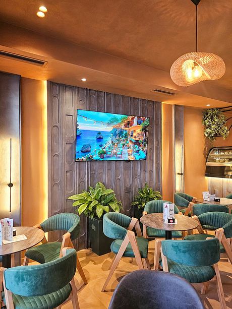 Cozy café interior with rustic wood paneling, plush green chairs, and a large wall-mounted TV.