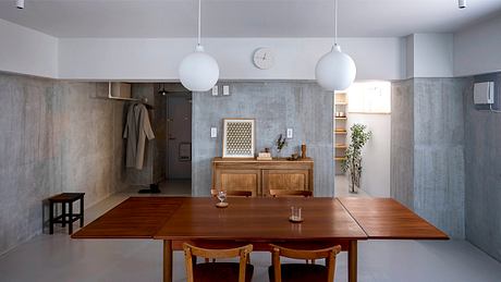 A minimalist dining space with concrete walls, wooden furniture, and globe pendant lights.