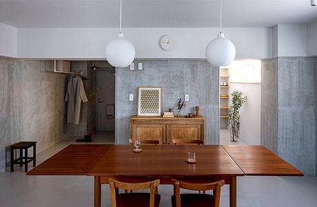 A minimalist dining space with concrete walls, wooden furniture, and globe pendant lights.