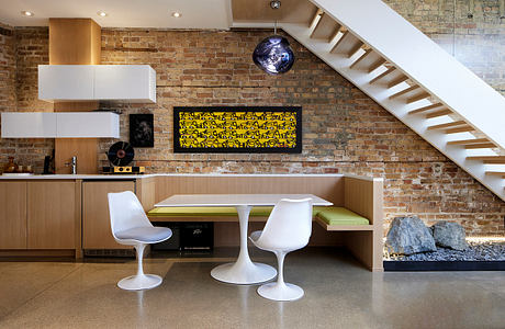 Spacious modern kitchen with exposed brick walls, built-in seating, and white minimalist furniture.