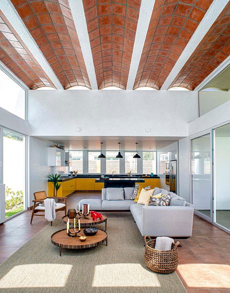 Spacious modern living area with vibrant yellow kitchen cabinets and exposed brick ceiling.