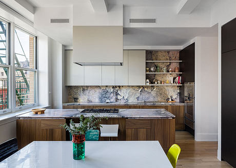 A bright, open kitchen with rustic stone walls, wooden cabinets, and a large marble countertop.