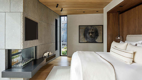 Modern bedroom with sleek fireplace, wooden ceiling, and large portrait artwork.