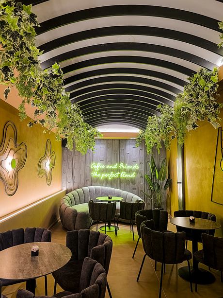 A vibrant, arched cafe interior with lush greenery, curved seating, and neon signage.