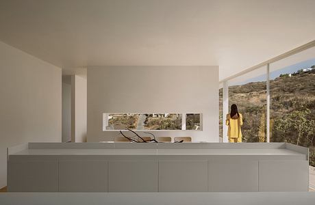 Minimalist modern interior with large windows overlooking a natural landscape.