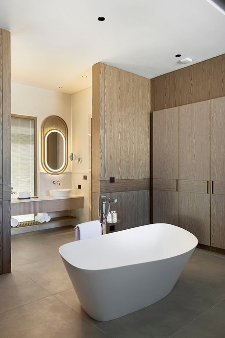 Elegant bathroom with freestanding tub, wooden vanity, and oval mirror. Minimalist design.