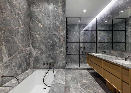 Luxurious bathroom with sleek marble walls, glass shower enclosure, and wooden cabinetry.