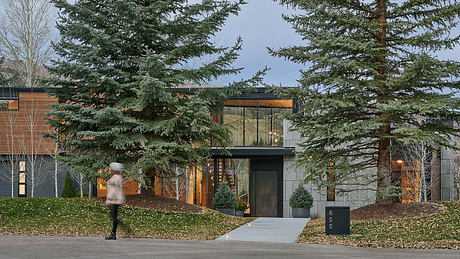 Contemporary mountain-style home with warm wood accents, glass facades, and towering evergreens.