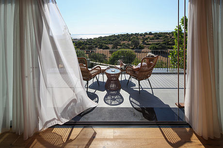 A sun-filled balcony with wicker furniture overlooking a scenic countryside.